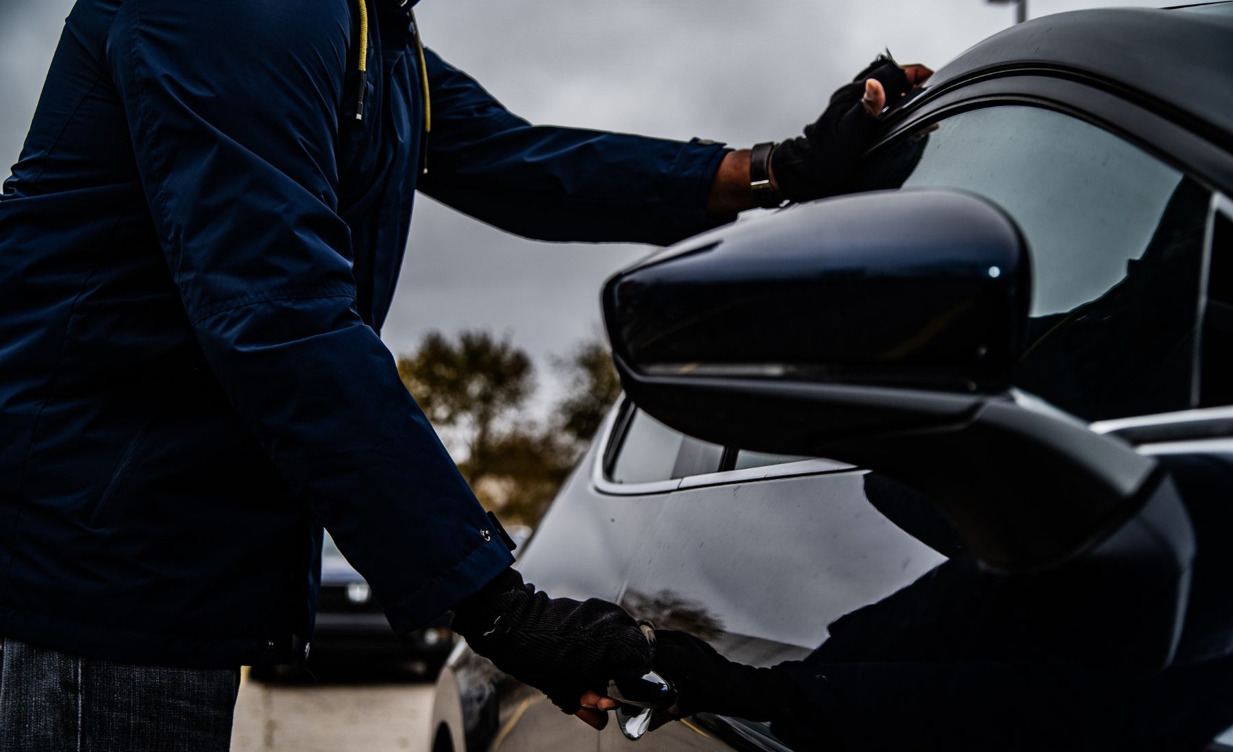 A man trying to steal a black car